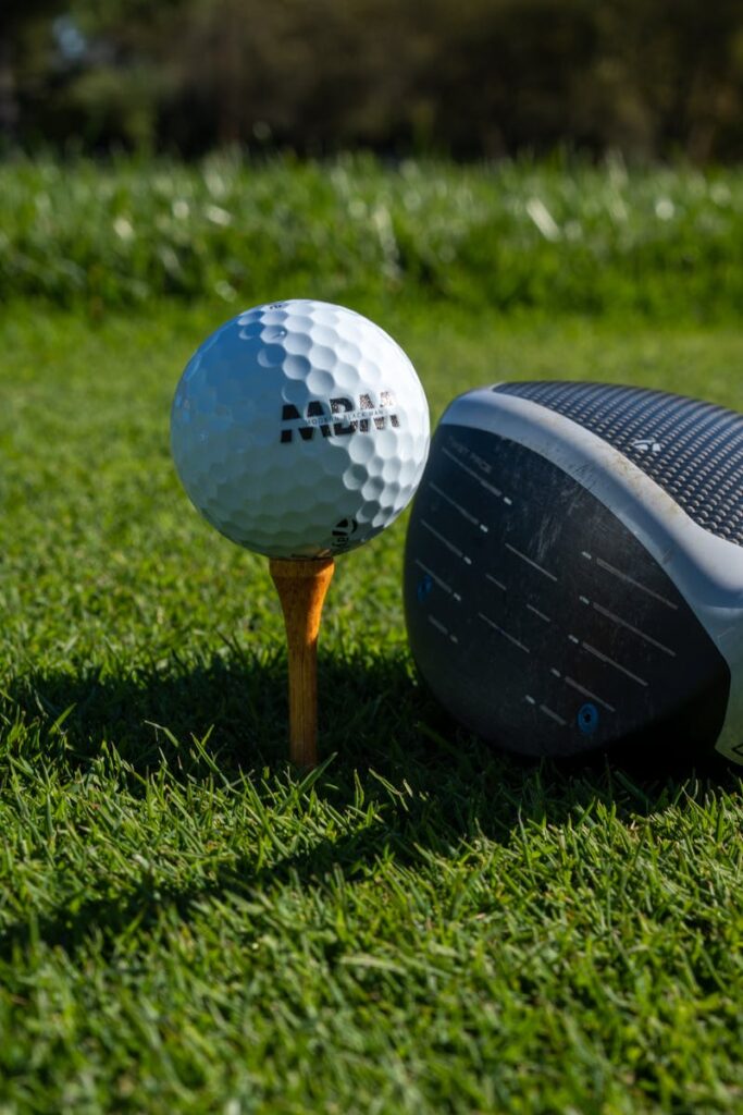 Close-up of a golf ball on a tee next to a club on a sunny day outdoors.